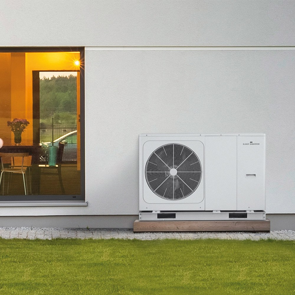 Air Source Heat Pump outside house, with stone wall behind it.